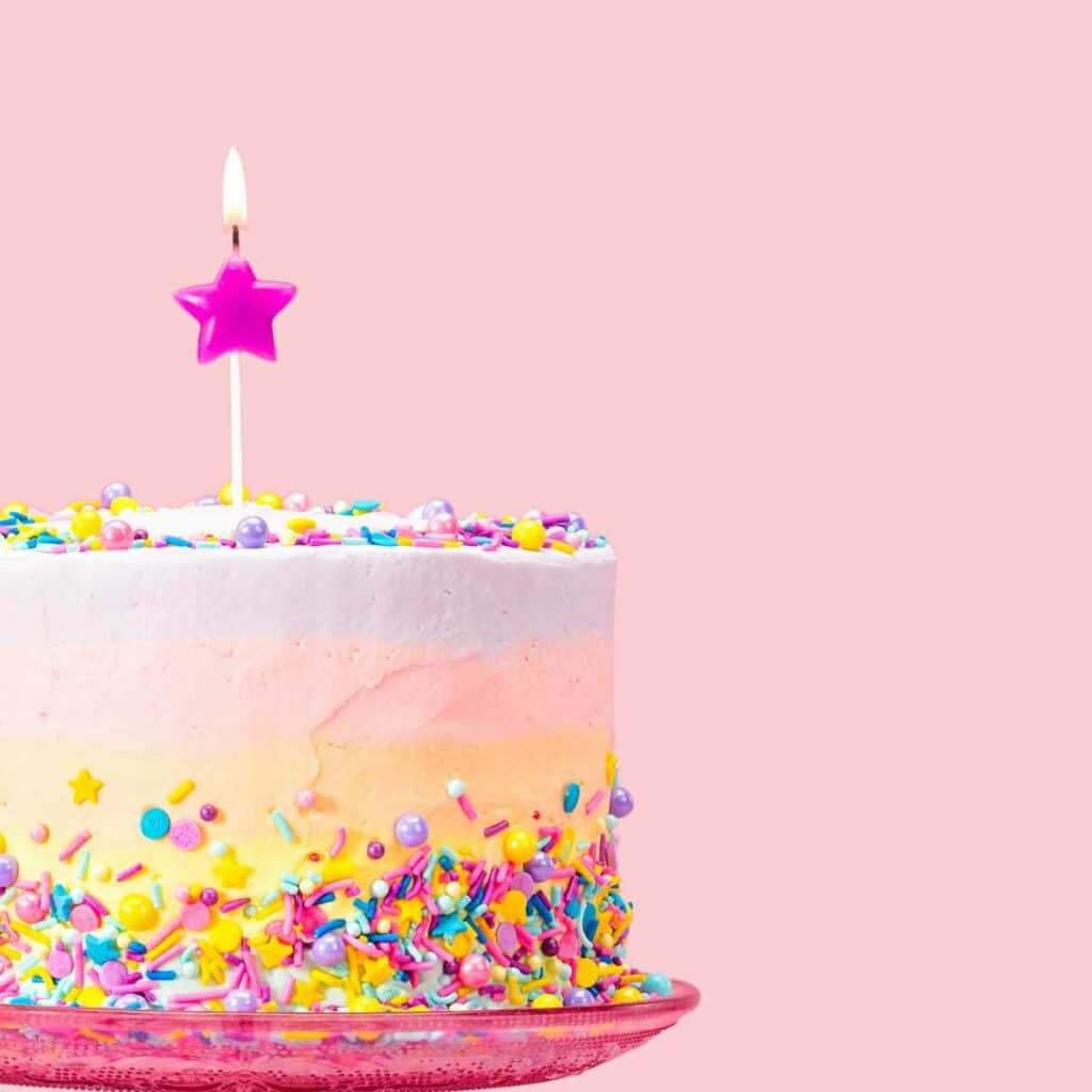 Pink birthday cake with frosting, sprinkles and a single candle.