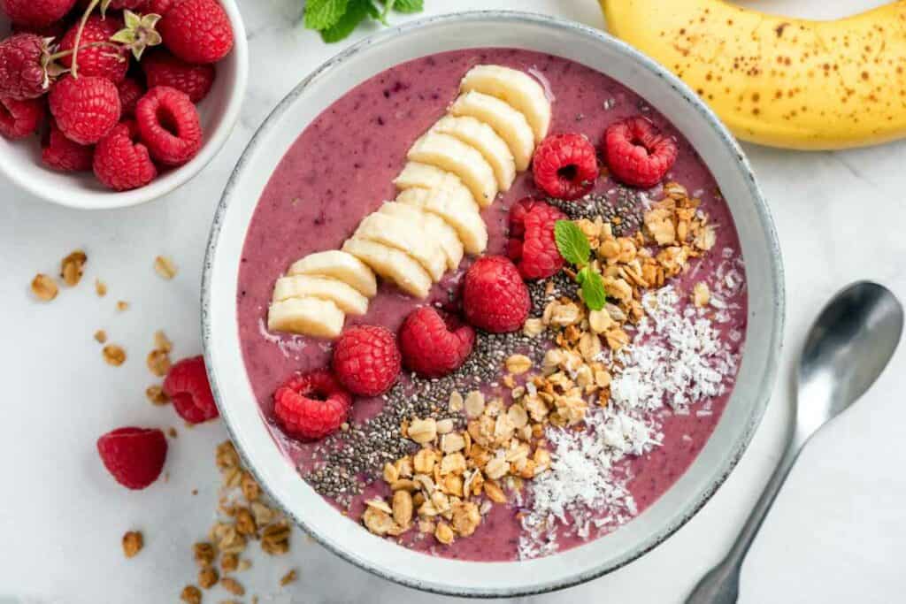 Berry smoothie bowl topped with banana, raspberries, chia seeds, muesli and coconut.