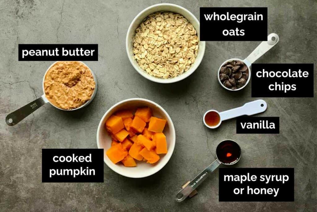 Ingredients for cookies in bowls and measuring cups on a dark grey marble kitchen bench.