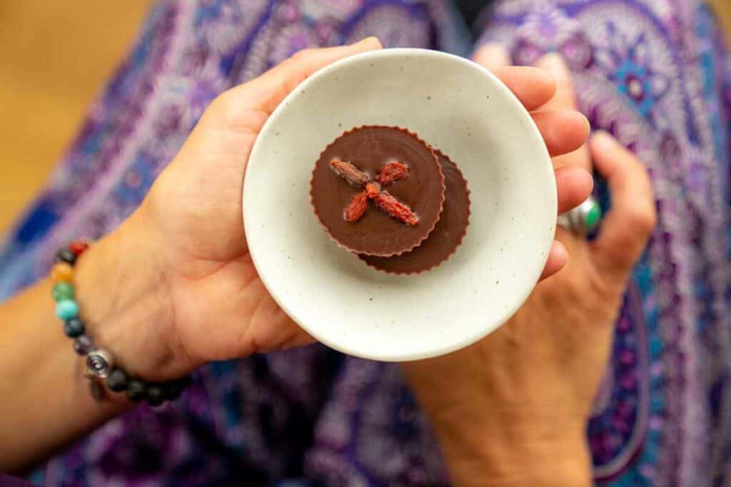 Two dark chocolates in a small bowl being cupped in a hand with colourful pants beneath.
