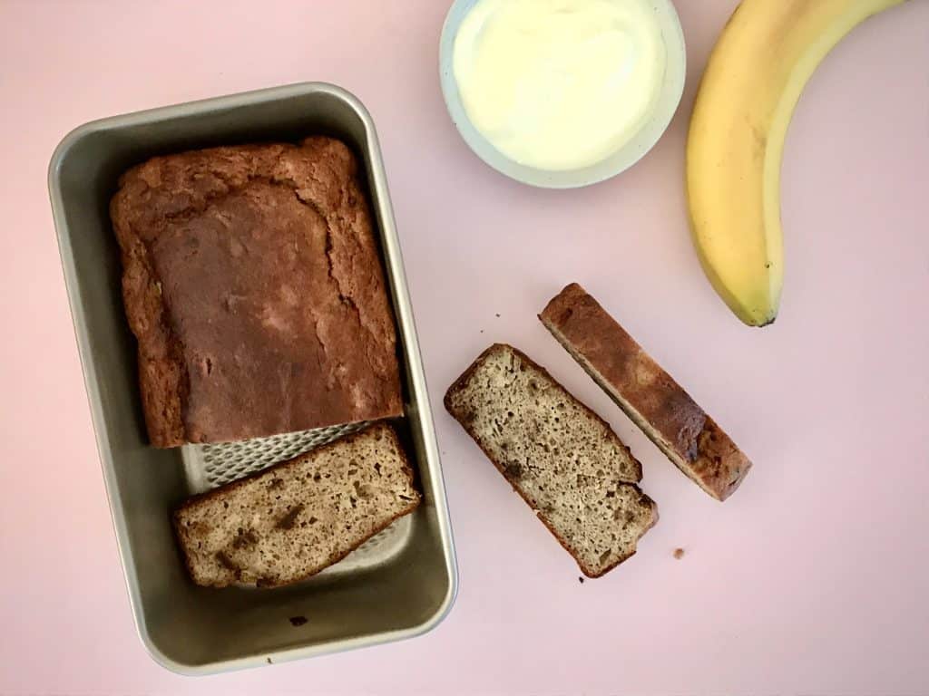 Loaf of sugar-free banana bread in tin with a few cut slices on kitchen bench top