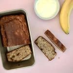 Loaf of sugar-free banana bread in tin with a few cut slices on kitchen bench top