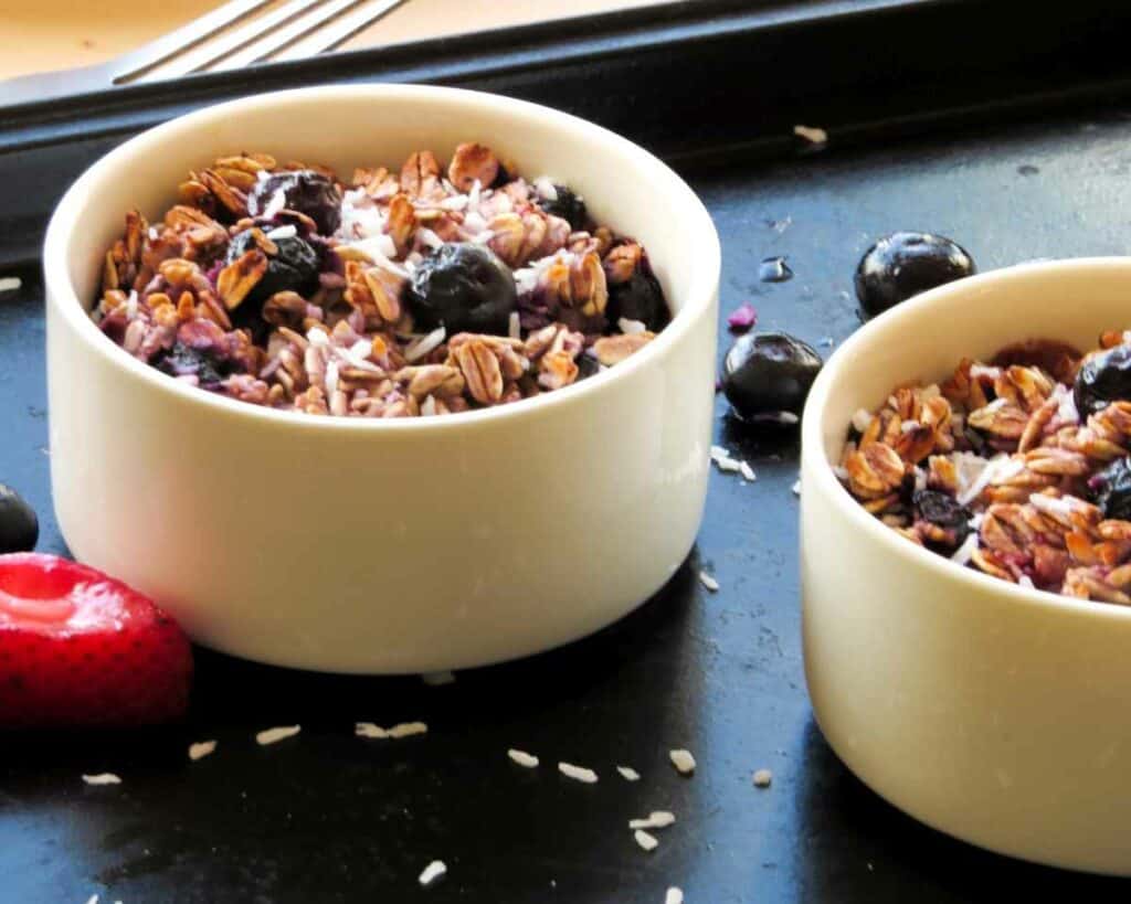 Two ramekins with berry baked oatmeal on a black baking tray.