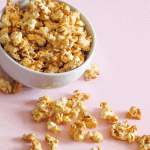 Caramel Popcorn tipped out of a white bowl on a pink surface