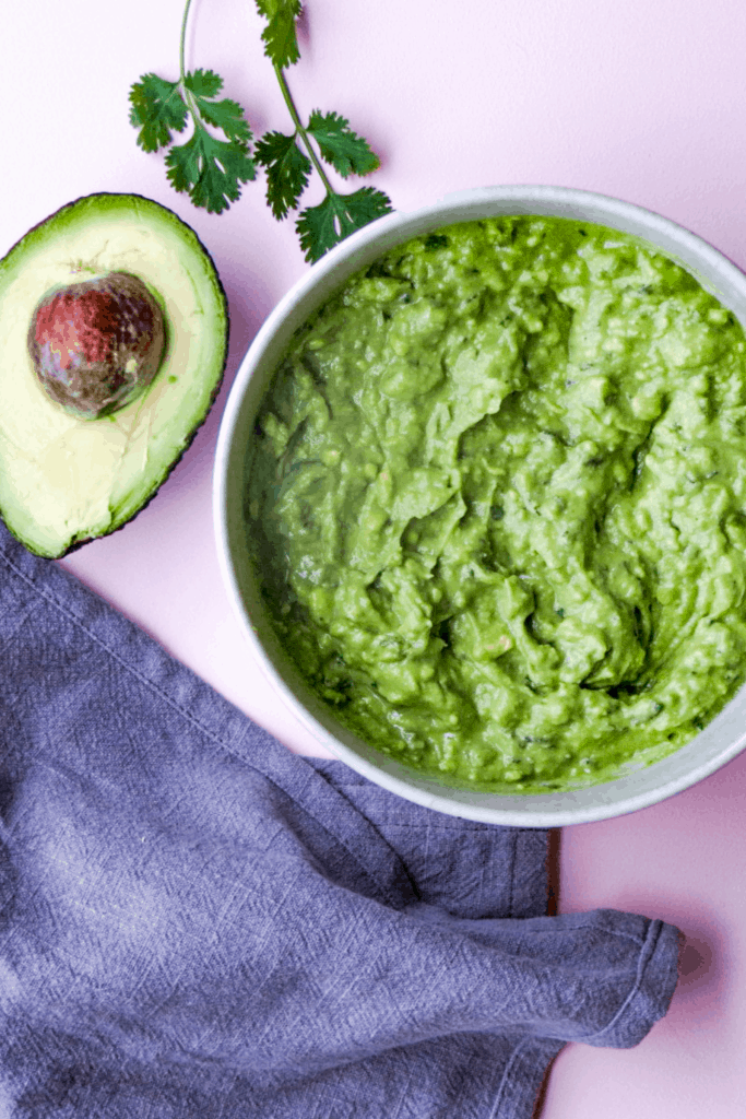 bowl guacamole on pink background with half an avocado
