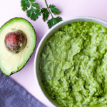 bowl guacamole on pink background with half an avocado