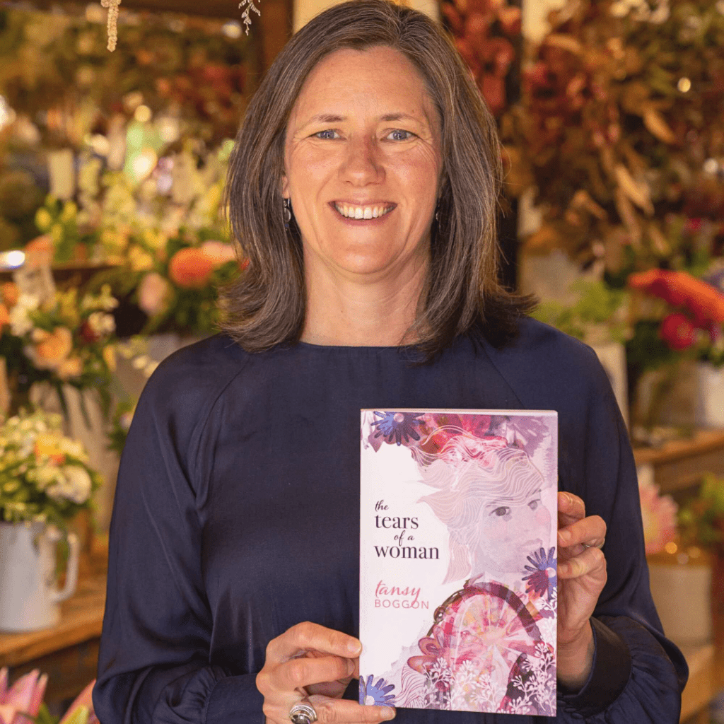 Tansy Boggon holding novel, The Tears of a Woman in a florist shop