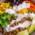 Brown rice served in a bowl with taco-seasoned beef, corn, black beans, fresh tomatoes, avocado, sour cream, lime juice and grated cheese.