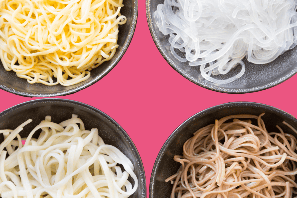 Four bowls on a pink background with egg noodles, vermicelli rice noodles, udon noodles and soba (buckwheat) noodles.