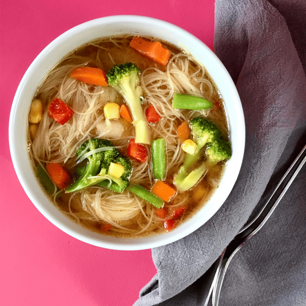 Bowl of noodle soup on pink background with grey tea towel