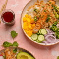A Buddha bowl with rice, salmon, cucumber, mango, radish, avocado and sweet sticky ginger sauce.