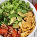 A grain bow with a mixture of rice, corn and black beans served alongside lettuce, avocado, crumbled corn and crumbled corn chips.
