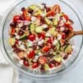 Quinoa salad with cherry tomatoes, cucumber, red onion, olives and feta in a glass bowl.