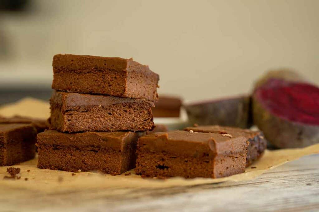 Slices of chocolate beetroot brownie on baking paper with a cut beetroot in background.
