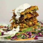 Stack of Carrot and Potato Fritters on coleslaw veggies with a drizzle of tzatziki.