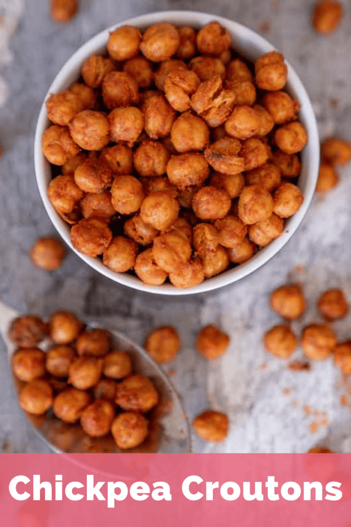 Crispy chickpeas in a small bowl on a sheet of baking paper with chickpeas spread over it and a spoonful of chickpeas.