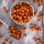 Crispy chickpeas in a small bowl on a sheet of baking paper with chickpeas spread over it and a spoonful of chickpeas.
