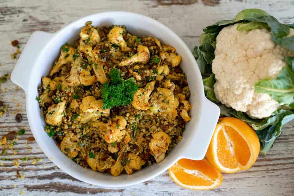 Roasted Cauliflower Quinoa Salad in large white serving dish on a kitchen bench with a cut orange and whole cauliflower beside it.