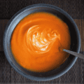 Overhead shot of Vegan Tomato Soup in a black bowl with spoon and swirl of yogurt.