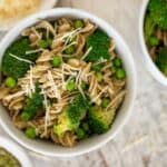 Bowl with vegetarian pesto pasta surrounded by Parmesan cheese, pesto and broccoli florets.