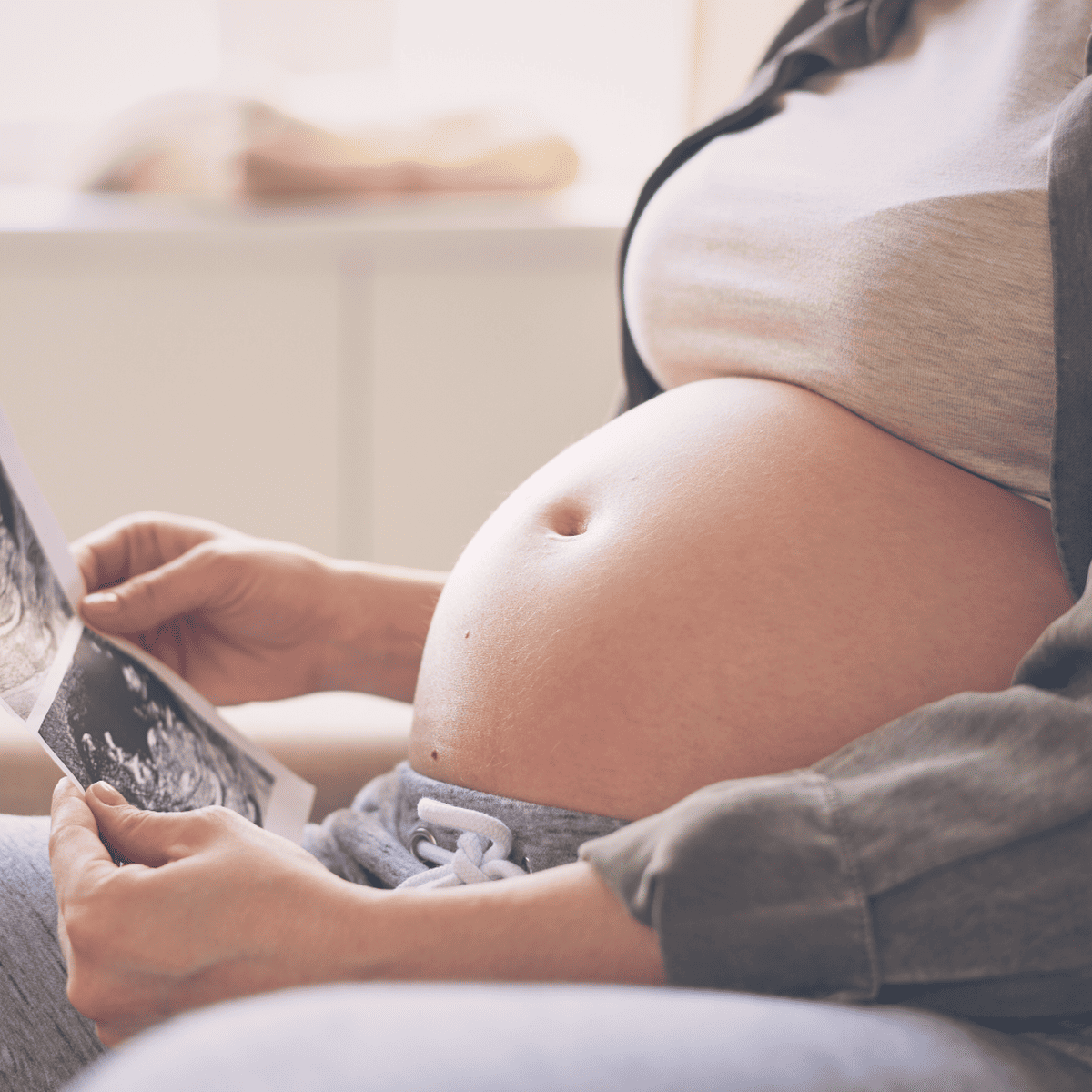 A woman sitting with her pregnant belly showing, looking at a printed sonogram image.
