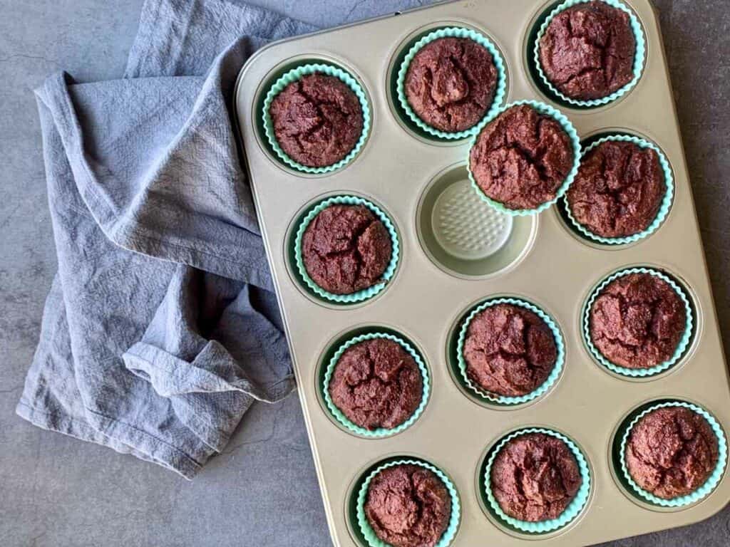 Tray of beetroot brownie muffins with teal blue silicone patty pans, on a dark grey kitchen bench with a grey tea towel.