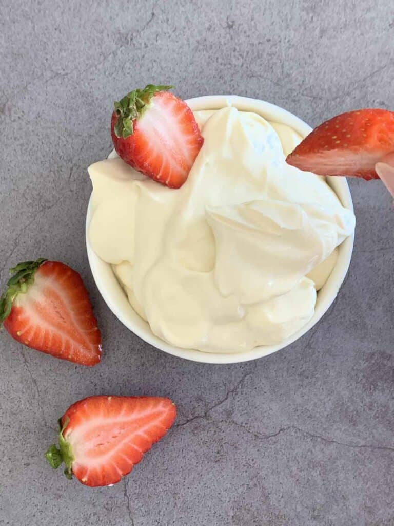 Greek Yogurt Cream Cheese Fruit Dip in a small bowl on a dark grey kitchen bench with four strawberry halves.