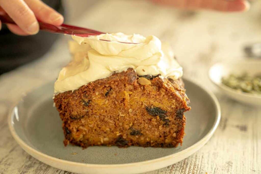 Greek yogurt frosting being spread onto pumpkin and prune loaf with a pink spatula. 