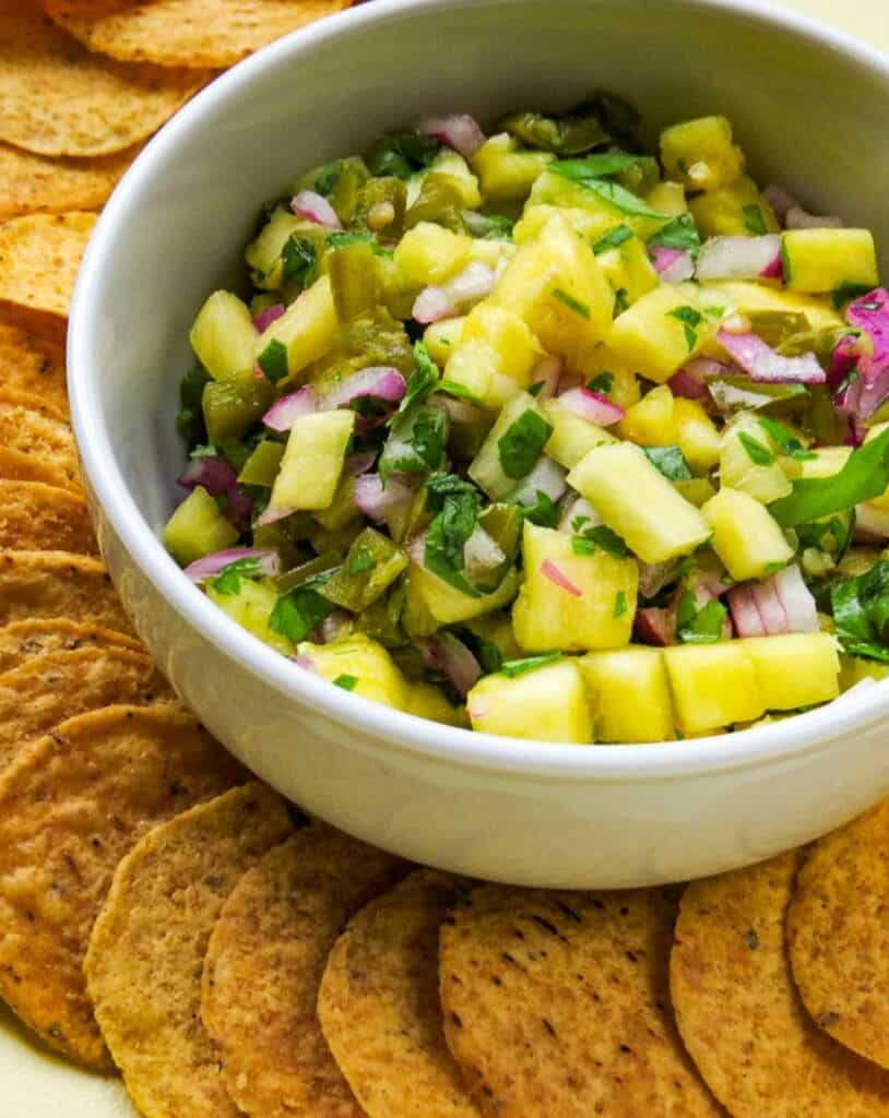 White bowl with pineapple salsa surrounded by corn chips.